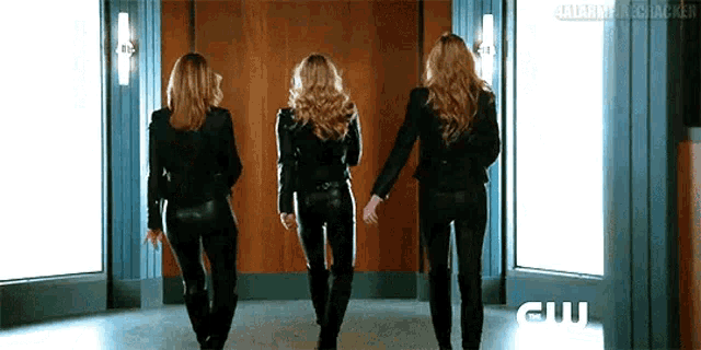three women in leather pants are walking in a hallway .