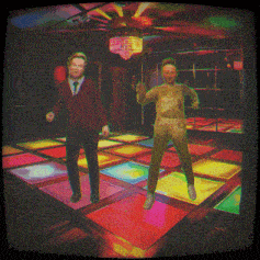 two people are dancing on a colorful dance floor in a dark room