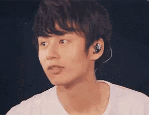 a young man wearing ear buds and a white shirt is looking at the camera .