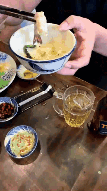 a person is holding chopsticks over a bowl of food with a bottle of beer on the table