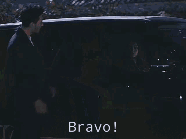 a man in a suit and white shirt says bravo in a dark room