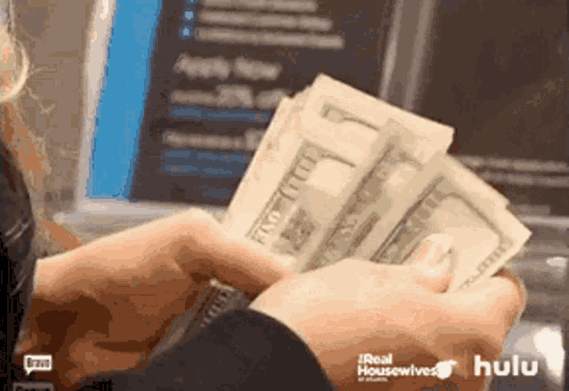 a person is holding a bunch of money in front of a laptop screen that says hulu
