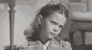 a black and white photo of a young girl in a suit making a serious face .