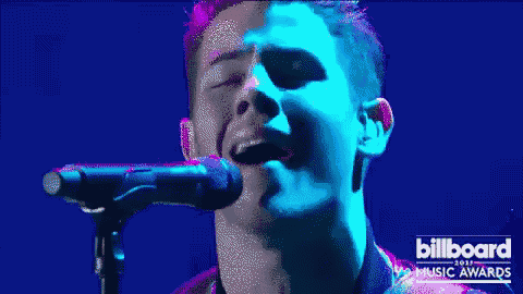 a close up of a man singing into a microphone with billboard music awards in the corner