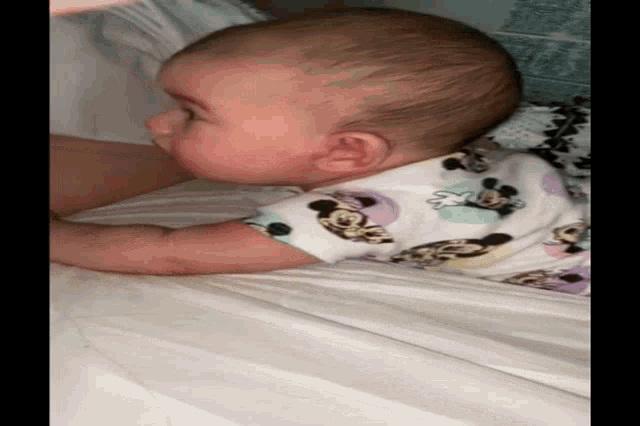 a baby wearing a mickey mouse outfit is sleeping on a bed