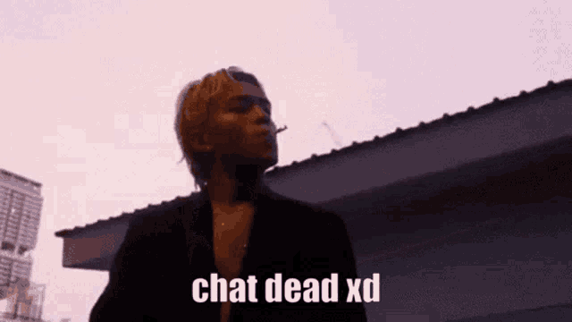 a man is smoking a cigarette in front of a building with the words chat dead xd written on the bottom .