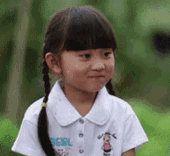 a little girl with pigtails is wearing a white shirt and making a face .