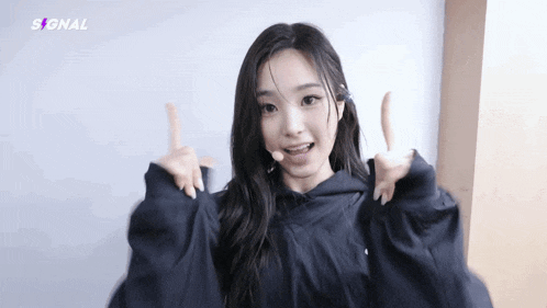 a young woman in a black hoodie is giving a thumbs up .
