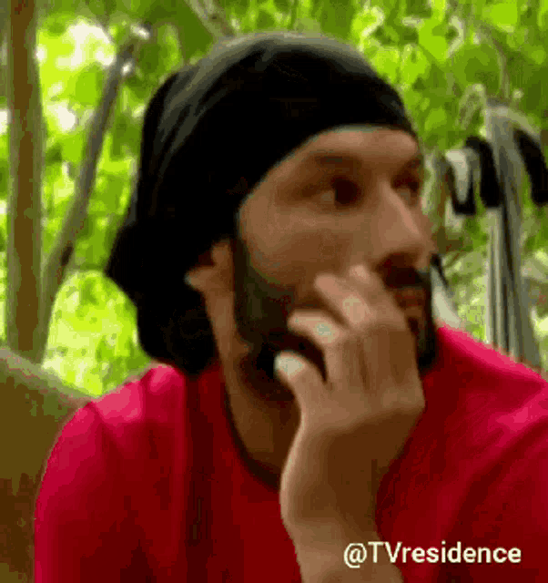 a man with a beard wearing a red shirt and a black headband is thinking .