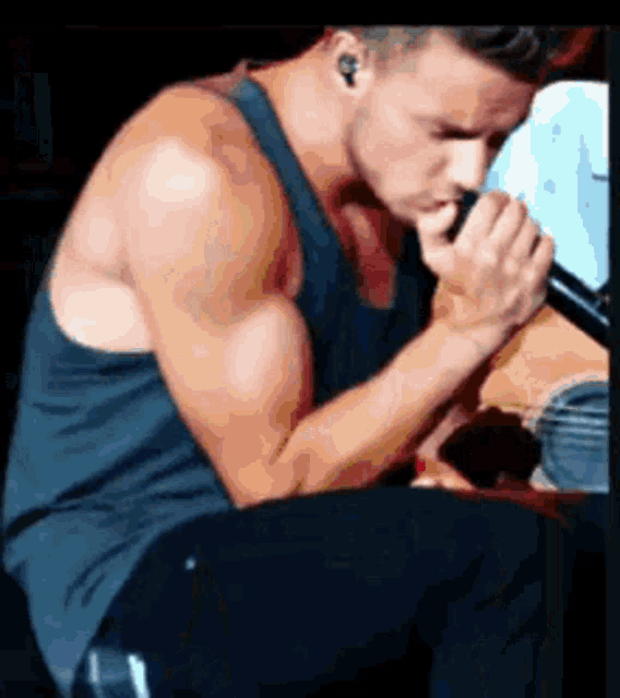 a man in a tank top is singing into a microphone while sitting down