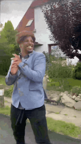a man in a blue jacket and hat is standing in front of a house .