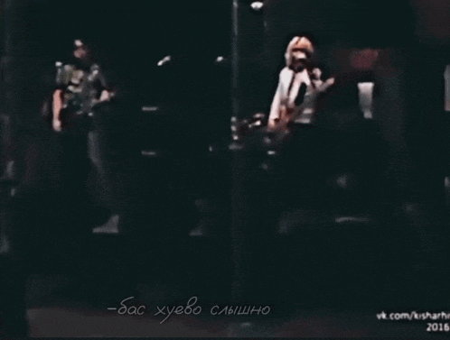a man singing into a microphone while another man plays a guitar in a dark room