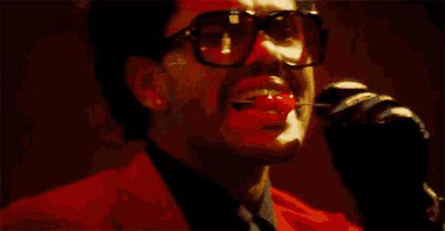 a close up of a man wearing glasses and a choker in a dark room .