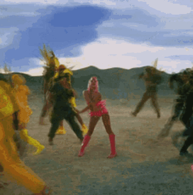a woman in a pink outfit is dancing in a field with other people