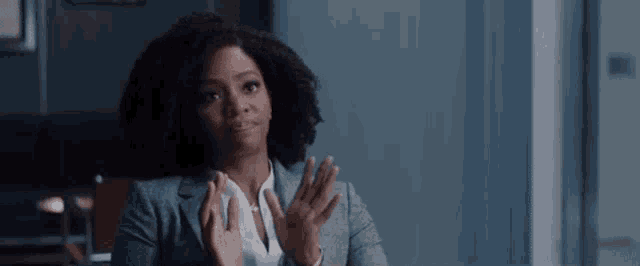 a woman in a suit is sitting at a table with her hands in the air .
