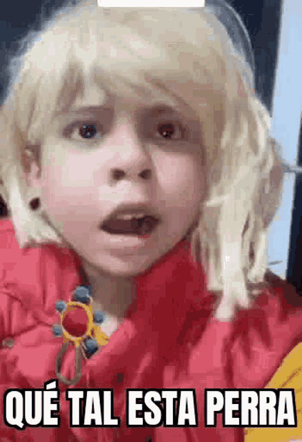 a little girl with blonde hair is wearing a red jacket and a wig .