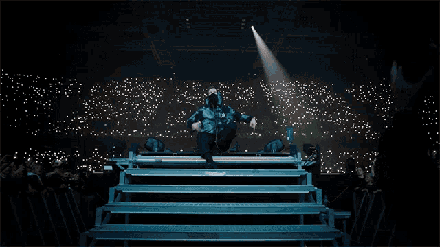 a man in a mask stands on a stage in front of a crowd of people
