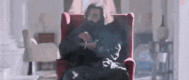 a man is sitting in a red chair smoking a cigarette .