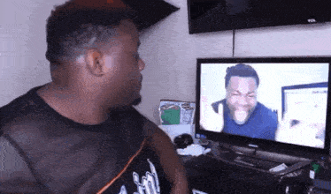 a man in a black tank top is looking at a tv screen