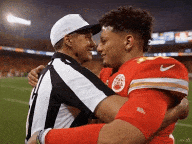 a referee is hugging a football player who is wearing a kansas city chiefs jersey