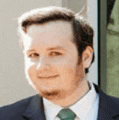 a man in a suit and tie is smiling while standing in front of a window .