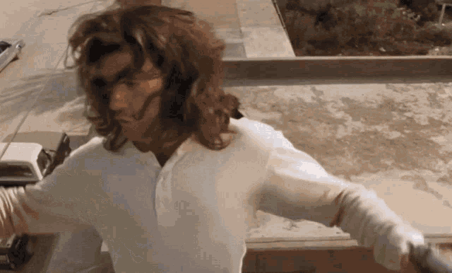 a man with long hair wearing a white shirt is standing on a balcony