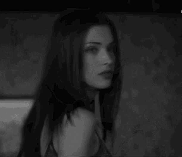 a black and white photo of a woman with long hair looking at the camera .