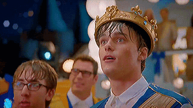 a man wearing a crown is standing in a room with other men .