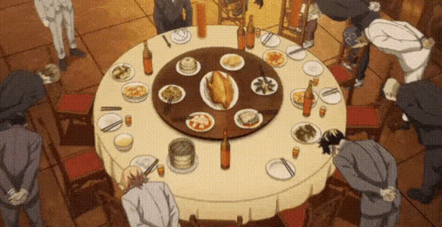 a group of people are sitting around a round table with plates of food and drinks on it .