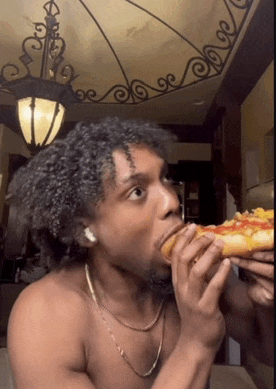 a shirtless man eating a slice of pizza