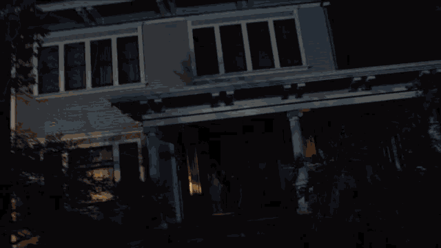 a man stands on the porch of a house at night looking out the window