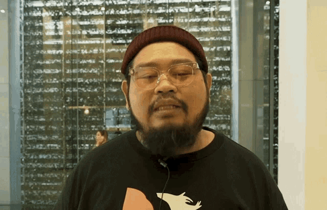 a man with a beard wearing glasses and a black shirt with a wolf on it