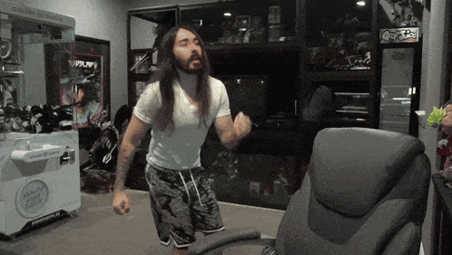 a man with long hair and a beard is standing in front of a chair and a claw machine that says capy tech on it