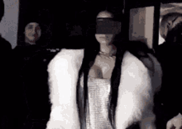 a woman wearing a white fur coat and blindfold is standing in front of a crowd .