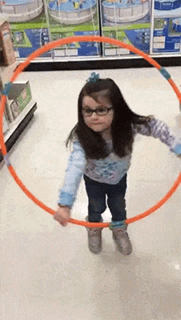a little girl wearing glasses is playing with a hula hoop in a store