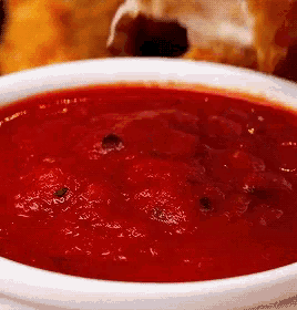 a close up of a bowl of tomato sauce on a plate