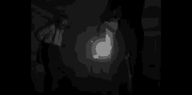 a black and white photo of two men standing in a dark room with a light in the background .