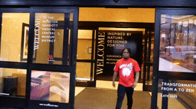 a man in a red shirt is standing in front of a sign that says " welcome "