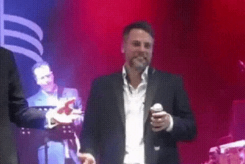 a man in a suit is singing into a microphone on stage