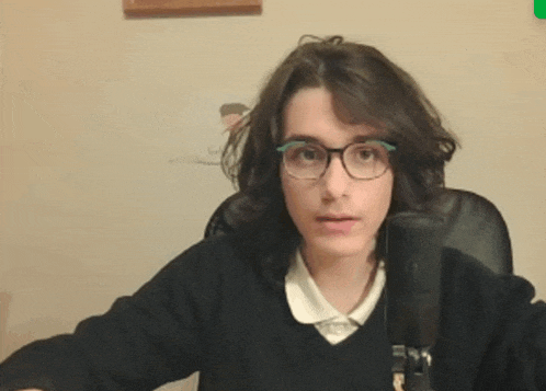a young woman wearing glasses and a black sweater sitting in front of a microphone