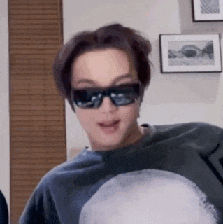 a young man wearing sunglasses and a sweatshirt is standing in a room .