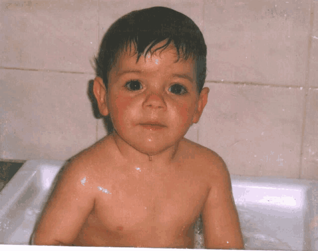 a shirtless child is taking a bath in a bathtub