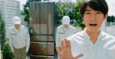 a man in a white shirt is standing in front of a refrigerator while two men in white uniforms are standing behind him .