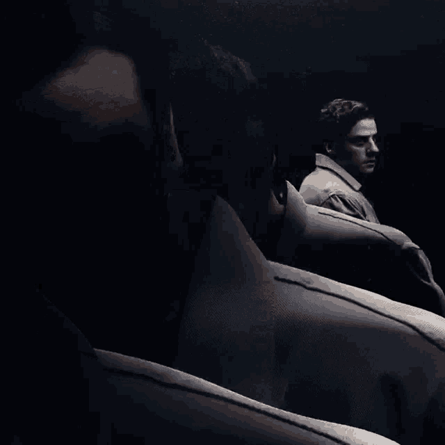 a man in a suit stands in the dark looking at his reflection in a mirror