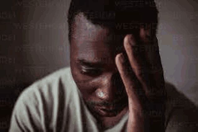 a man is holding his head with his hand while looking down .