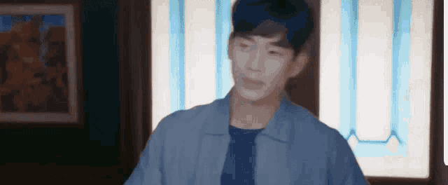 a young man in a blue jacket is standing in front of a window in a room .