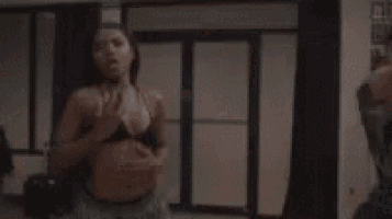 two women are standing next to each other in a room and one is wearing a bikini top .