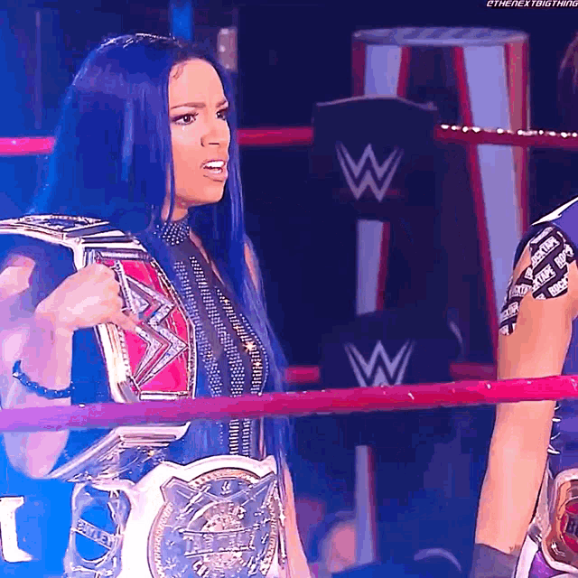a woman with blue hair is holding a wrestling championship belt in a ring