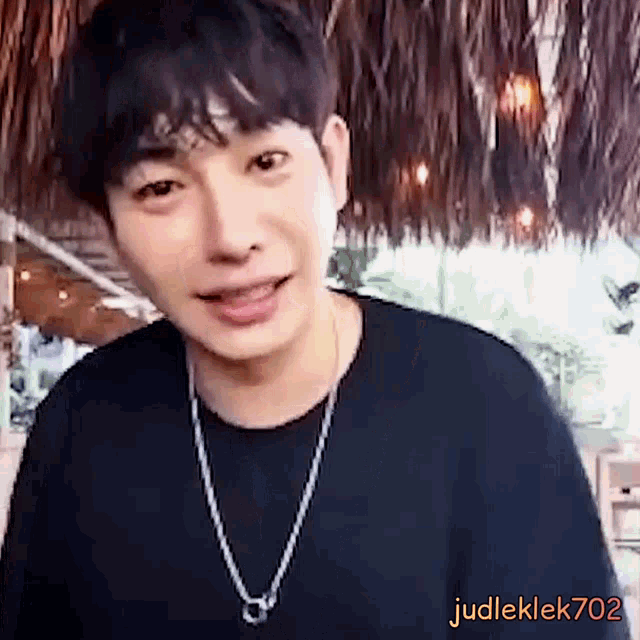 a young man wearing a black shirt and a silver chain necklace is smiling .