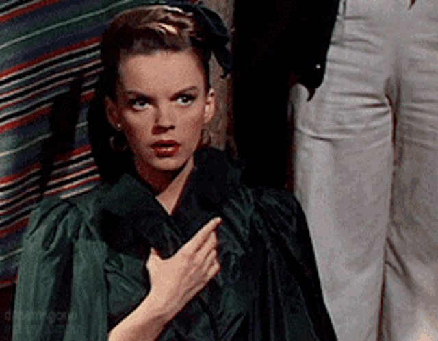 a woman in a green dress is pointing her finger at her chest
